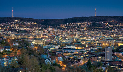 Obraz premium Panoramic view of Stuttgart city center in Germany during spring with warm golden evening light. Dense urban architecture, hills and residential districts captured from an elevated viewpoint.