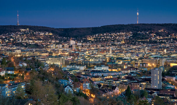 Panoramic view of Stuttgart city center in Germany during spring with warm golden evening light. Dense urban architecture, hills and residential districts captured from an elevated viewpoint.