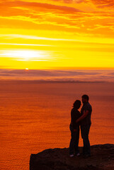 Fototapeta premium Couple watching dramatic sunset from Bolafjall cliff in Westfjords Iceland with glowing sky over ocean