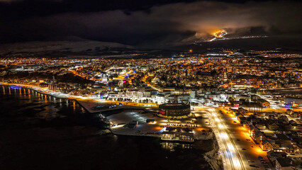 Fototapeta premium Drone view of Akureyri in North Iceland at night with illuminated bridge and city lights reflecting on water. Beautiful aerial scene of Akureyri harbor showing urban landscape and coastline in Iceland