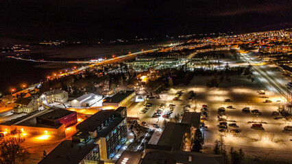 Fototapeta premium Drone view of Akureyri in North Iceland at night with illuminated bridge and city lights reflecting on water. Beautiful aerial scene of Akureyri harbor showing urban landscape and coastline in Iceland