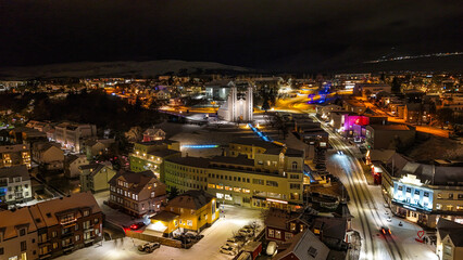 Fototapeta premium Drone view of Akureyri in North Iceland at night with illuminated bridge and city lights reflecting on water. Beautiful aerial scene of Akureyri harbor showing urban landscape and coastline in Iceland