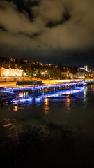 Fototapeta premium Drone view of Akureyri in North Iceland at night with illuminated bridge and city lights reflecting on water. Beautiful aerial scene of Akureyri harbor showing urban landscape and coastline in Iceland