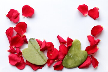 Red rose petals and jade gua sha on a white background close-up © Tkathenko
