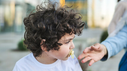 Obraz premium Boy with curly hair and pacifier extending hand towards an adult's outstretched arm