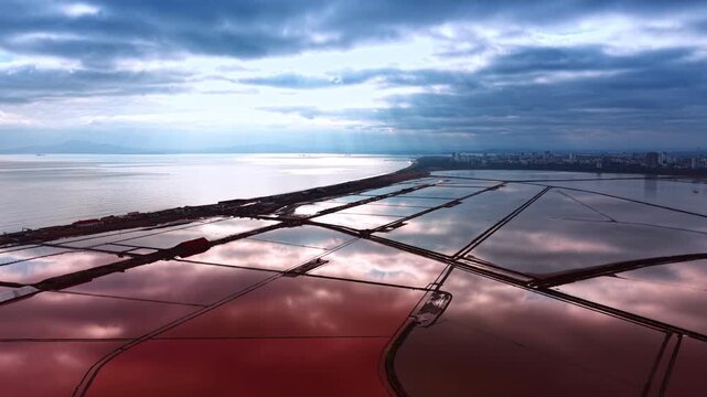 Beautiful cloudy sky reflects in the vast seascape and waterscape of pink lakes. Drone flight over the saline lakes for salt production.