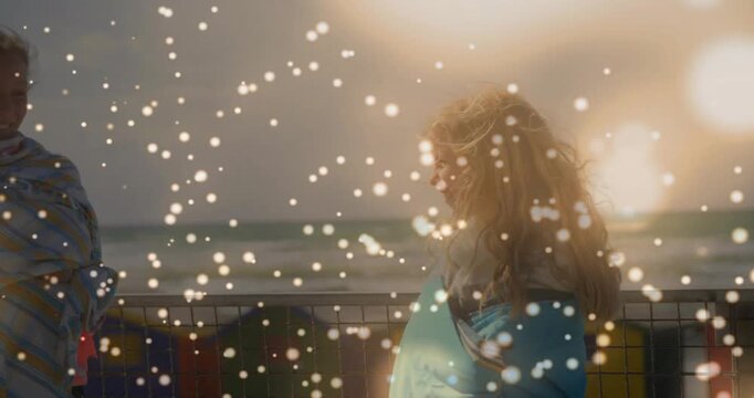 Blonde child in blue towel turning toward friend as striped towel child appearing, greeting on pier