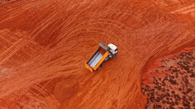 Yellow truck has thrown down the red spoil from the basket. Top view on the vehicle working in the area with red ground.