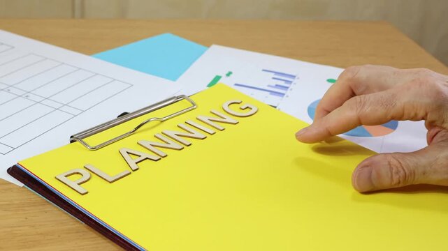 Wooden sign PLANNING with a man's hand scrolling over a planning form, office work concept.