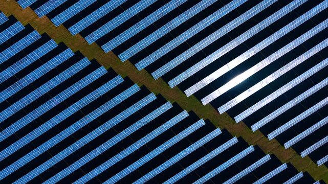 Top down view of solar panels with sun reflection. Geometric aerial pattern of photovoltaic rows with a bright glint of sunlight on the surface.