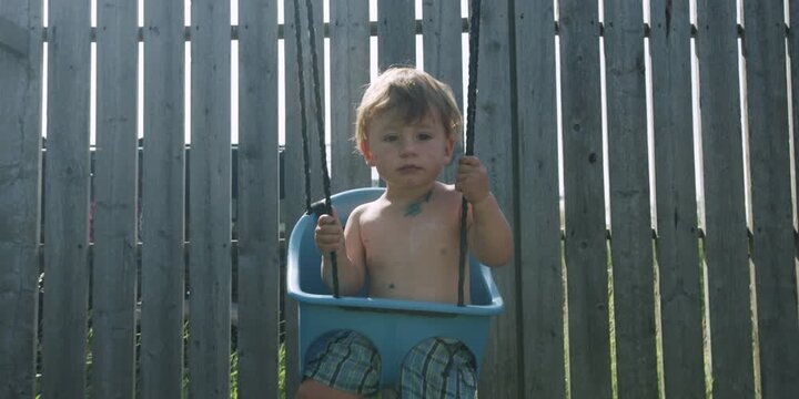 Little toddler sitting in a swing outside in a backyard