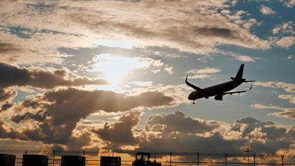 Fototapeta premium Passenger airplane landing at sunset in cloudy sky