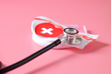 Stethoscope with nurse hat on color background.