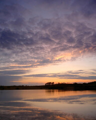 Obraz premium Spring sunset over Lake Lysek in Biskupiec, Poland. The calm water reflects beautiful shaped clouds of the sky.