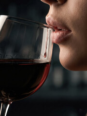 Woman sips red wine from glass in dark bar setting at night