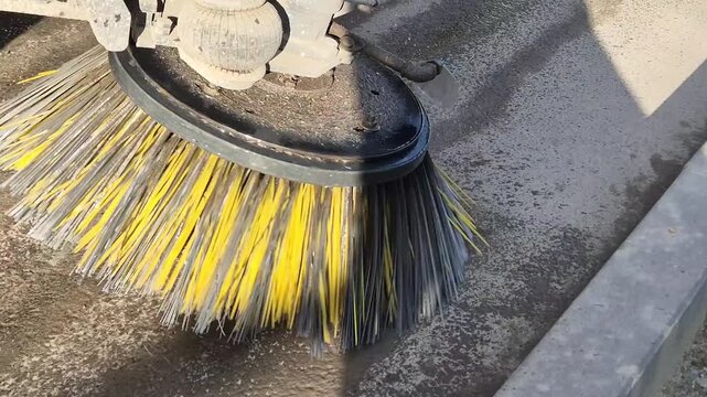 Close-up of a construction road sweeper truck brush rotating and spraying water to clean dust on a building site.