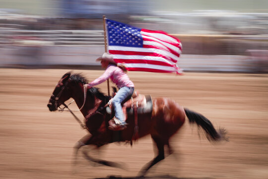 Galisteo, New Mexico, United States.  39th annual small town Galisteo authentic old western rodeo. Rodeo queen rides through arena with American flag. Blur effect.