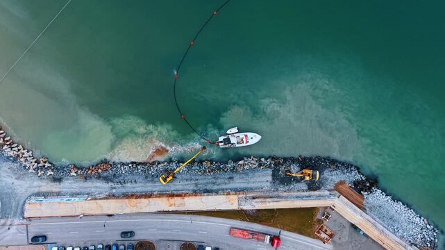 Aerial top down view of shoreline dredging and boat. Heavy machinery working on a rocky coast with boat and floating boom.