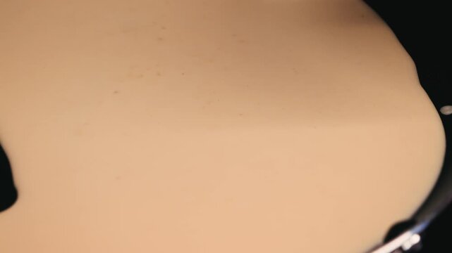 A close-up of liquid pancake batter being poured from a ladle onto a preheated pan. Cooking homemade crepes or pancakes. High quality 4k footage