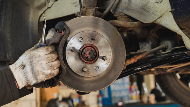 Mechanic changing car brake pads and disk, providing automotive repair in Moscow