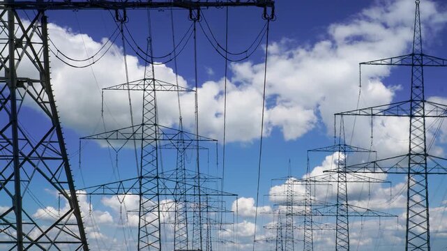 Wolken im Zeitraffer hinter den Stromleitungen und Strommasten einer Starkstrom &Uuml;berlandleitung - FOTOMONTAGE