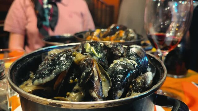 A steaming pot of freshly cooked mussels served hot and ready to eat. The mussels are prepared in a fragrant white wine and onion sauce, creating a rich and appetizing aroma. High quality 4k footage