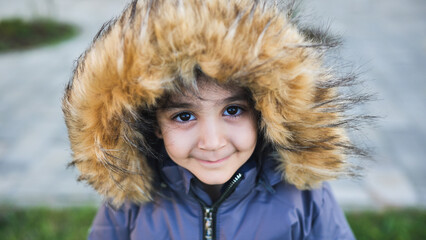 Child playing outdoors wearing a warm winter coat with fur hood, smiling at camera © Довидович Михаил