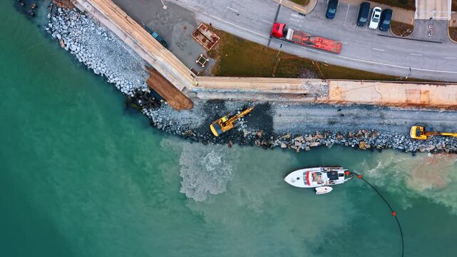 Drone view of excavator and dredging vessel at shore. Shoreline construction featuring heavy machinery and boat.