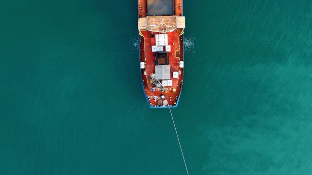 Overhead view of industrial ship deck in turquoise ocean. Symmetrical top down shot of a red and blue industrial vessel deck floating in clear turquoise sea water.
