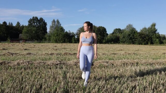 A woman in sportswear walks through a field in a village on a sunny summer day