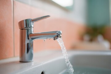 Chrome faucet running water bathroom sink closeup with orange tile background modern tap stream hygiene