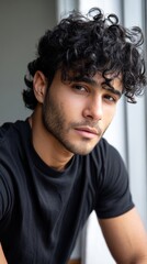 Fototapeta premium Half-body shot of a confident young man with black curly hair, staring into the camera with intensity, great for advertisements and modern media 
