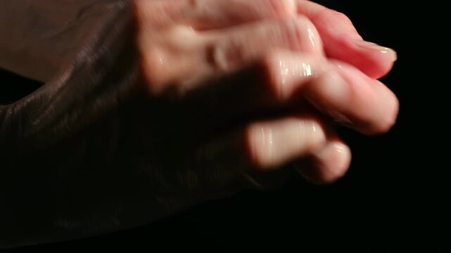 Close up person hands covered in oil or lotion being rubbed together, preparing for massage against dark background, skin care and relaxation concepts. Person rubbing oily hands together for massage