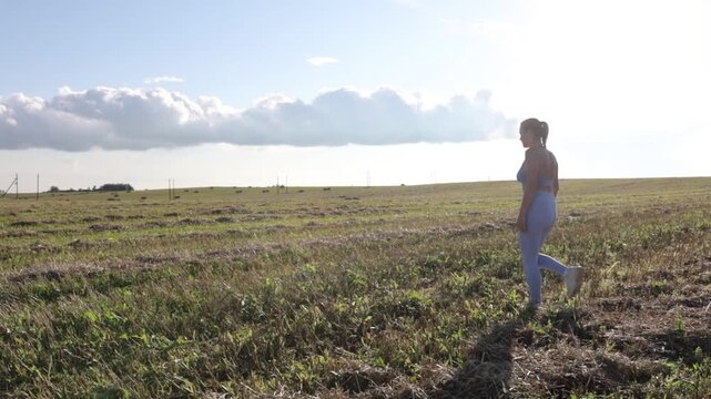 A woman in sportswear walks through a field in a village on a sunny summer day