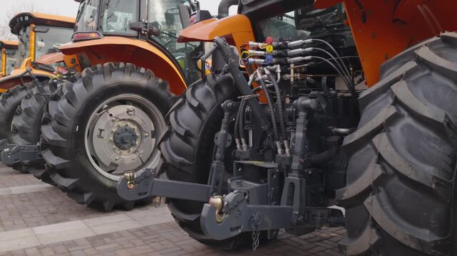 Many new orange agricultural tractors are parked close together in long line, with their large, rugged tires and rear hydraulic equipment clearly visible, representing modern farming machinery