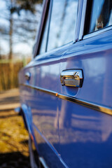 Close-up of a blue vintage car front: headlights, chrome grille and retro whitewall tires on a cobblestone road.