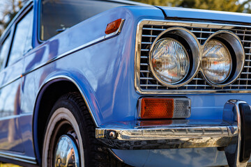 Fototapeta premium Close-up of a blue vintage car front: headlights, chrome grille and retro whitewall tires on a cobblestone road.