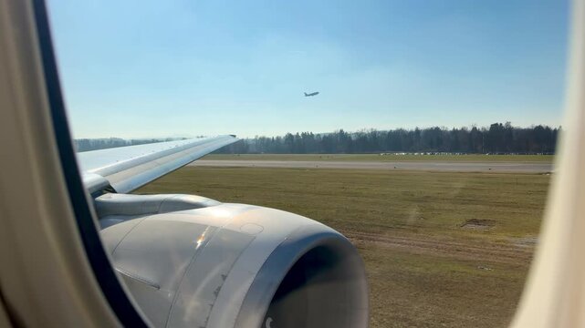 View from an airplane window during takeoff at Zurich Airport on a bright sunny day, runway and landscape visible below.