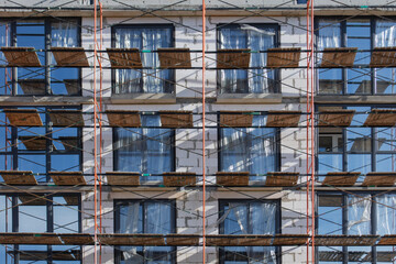 Obraz premium Residential building facade under construction with metal scaffolding and windows. Urban renovation and construction process concept showing apartment building development and exterior work.