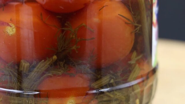 Canned pickled red tomatoes and herbs in a glass jar, rotating, close-up.