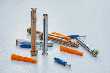 Variety of metal expansion anchors, sleeve anchors, nylon wall plugs, and screw-in anchors scattered on a light wooden surface. Different types and sizes of concrete and masonry fastening hardware. © vadish