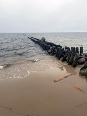 Fototapeta premium Wooden breakwater and stone path extending into the sea. Coastal erosion protection structure on sandy beach. Calm landscape of Baltic coast shore. Marine scenery with horizon line.