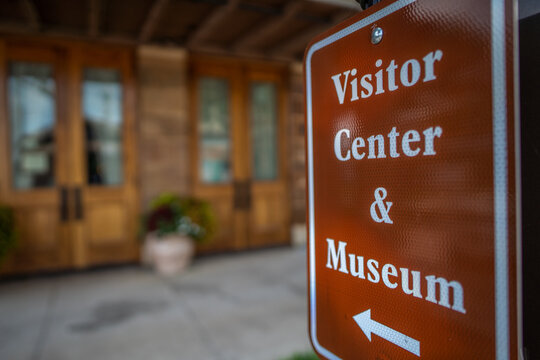 Close Up of Visitor Center and Museum Sign Pointing Towards Wooden Building 