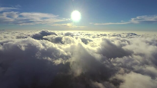 Aerial view from a dreamy, late afternoon flight above fluffy clouds while aimed directly at the sun for a while, and then ending with an angled right turn completely away from the sun.