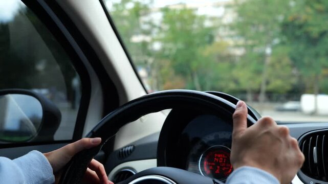 Close up of female hands spinning steering wheel driving a car practicing in city. Woman driver hands on steering wheel turning left practicing driving skill on parking. Slow motion.