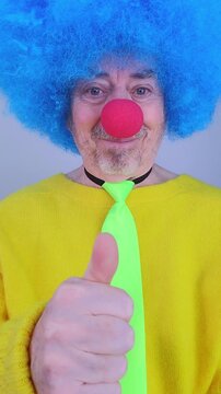 Close up of a smiling clown giving a thumbs up and pointing at the camera on a white background