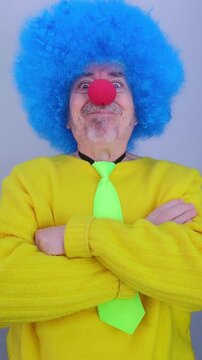 Serious man in a colorful clown costume with a blue wig suddenly making a funny face and smiling