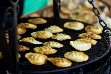 traditional smoked sheep cheese from Zakopane, Poland, being grilled on a large cast iron pan at a market. The cheese is shown during cooking, with a golden crust forming on the surface © Point of view