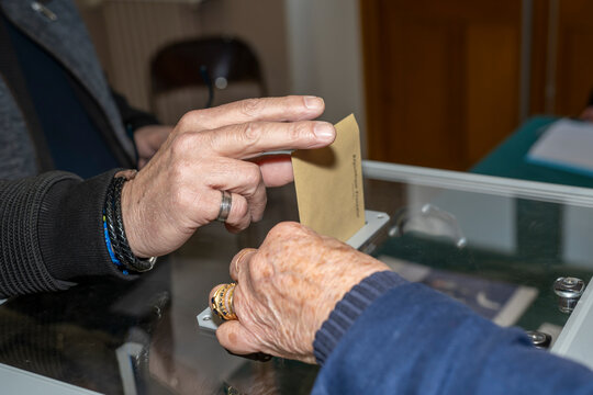 main d'un votant mettant une enveloppe dans une urne devant un assesseur.