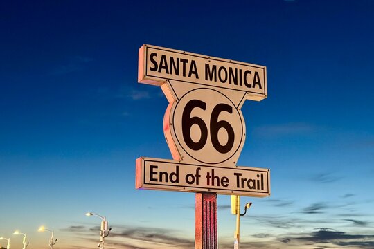Santa Monica, USA - February 27, 2026: Famous &ldquo;Santa Monica Route 66 End of the Trail&rdquo; sign at the pier amusement park at night, surrounded by visitors and bright lights.